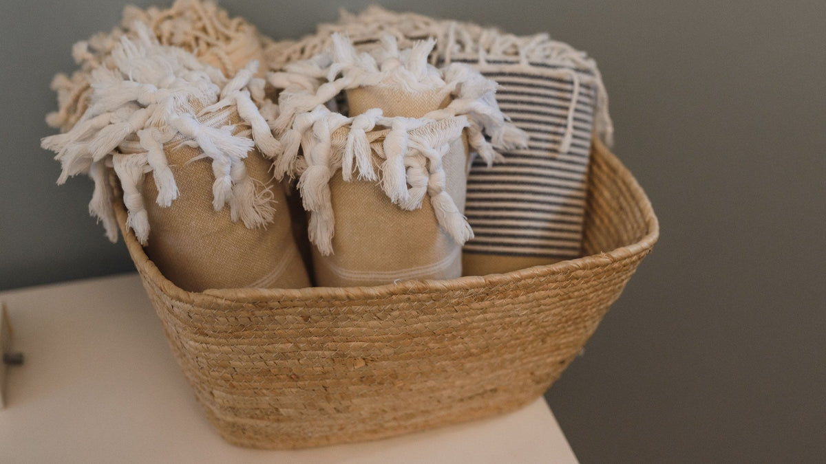 Three throw blankets rolled and standing upright in a woven basket with a wide flared rim
