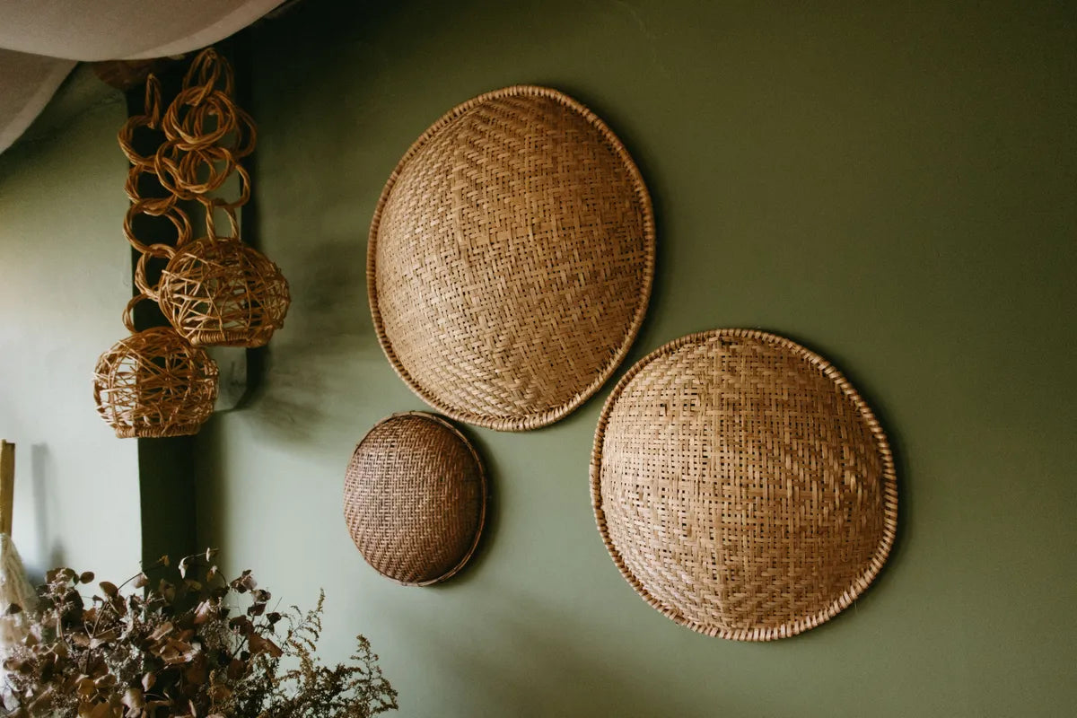 Three shallow woven basket trays in different sizes, hung together as a group on a sage green wall.