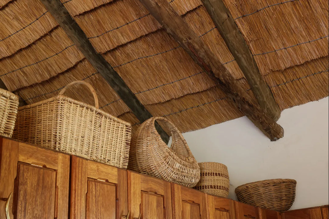 Handwoven natural fiber baskets stored along the top of a wooden cabinet beneath a thatched roof.