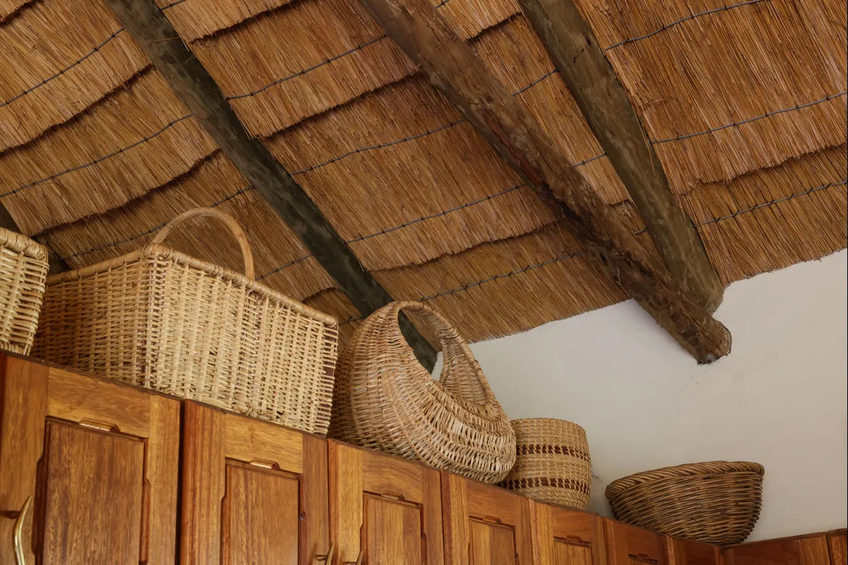 Handwoven natural fiber baskets stored along the top of a wooden cabinet beneath a thatched roof.