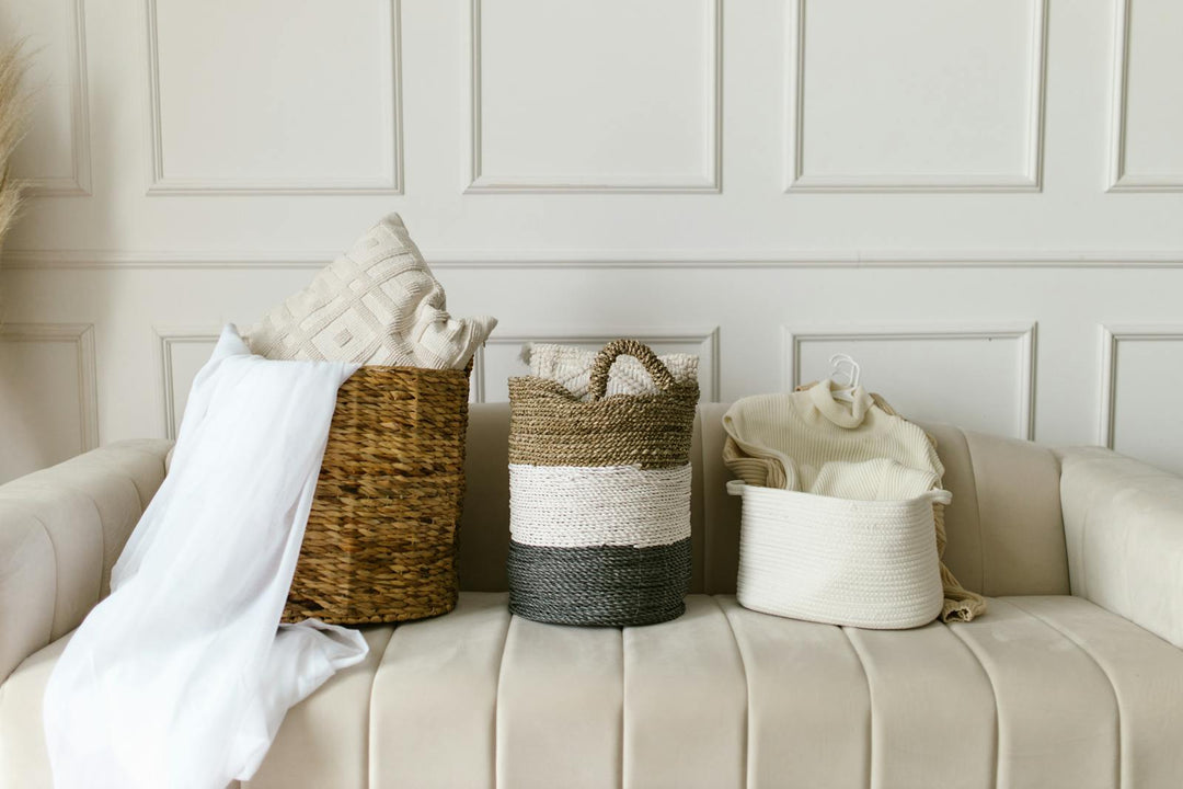 Three handwoven seagrass and jute storage baskets styled with linens on a cream sofa