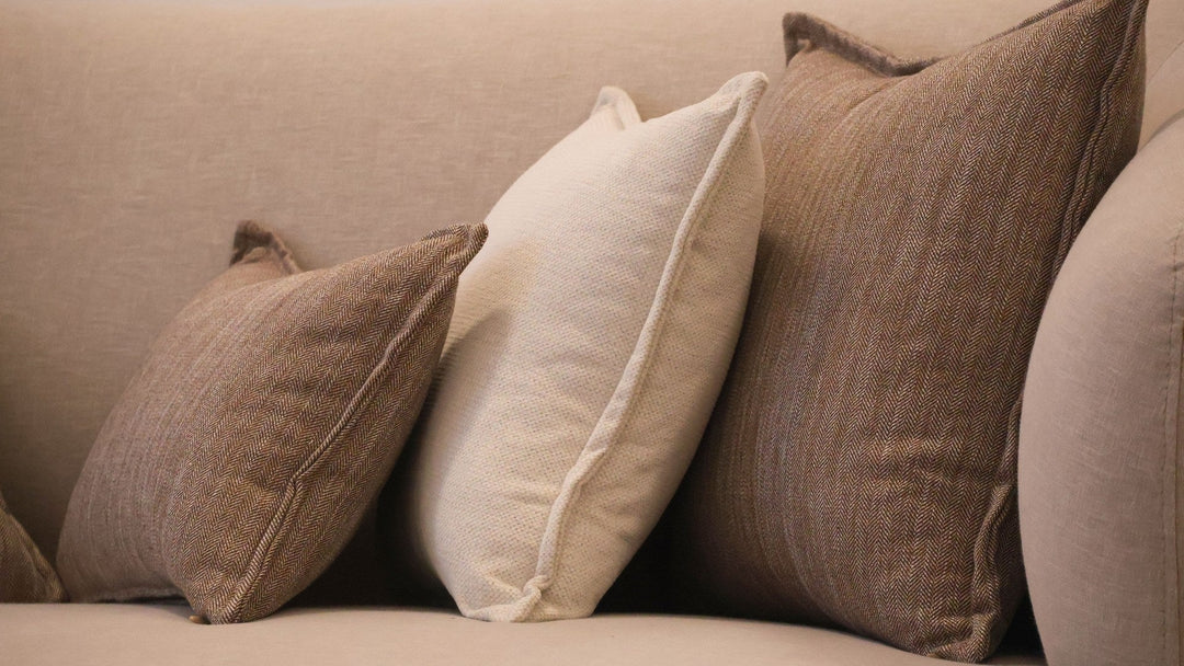 Pillows in textured natural covers resting against the back of a linen sofa, corners filled and slightly rounded.