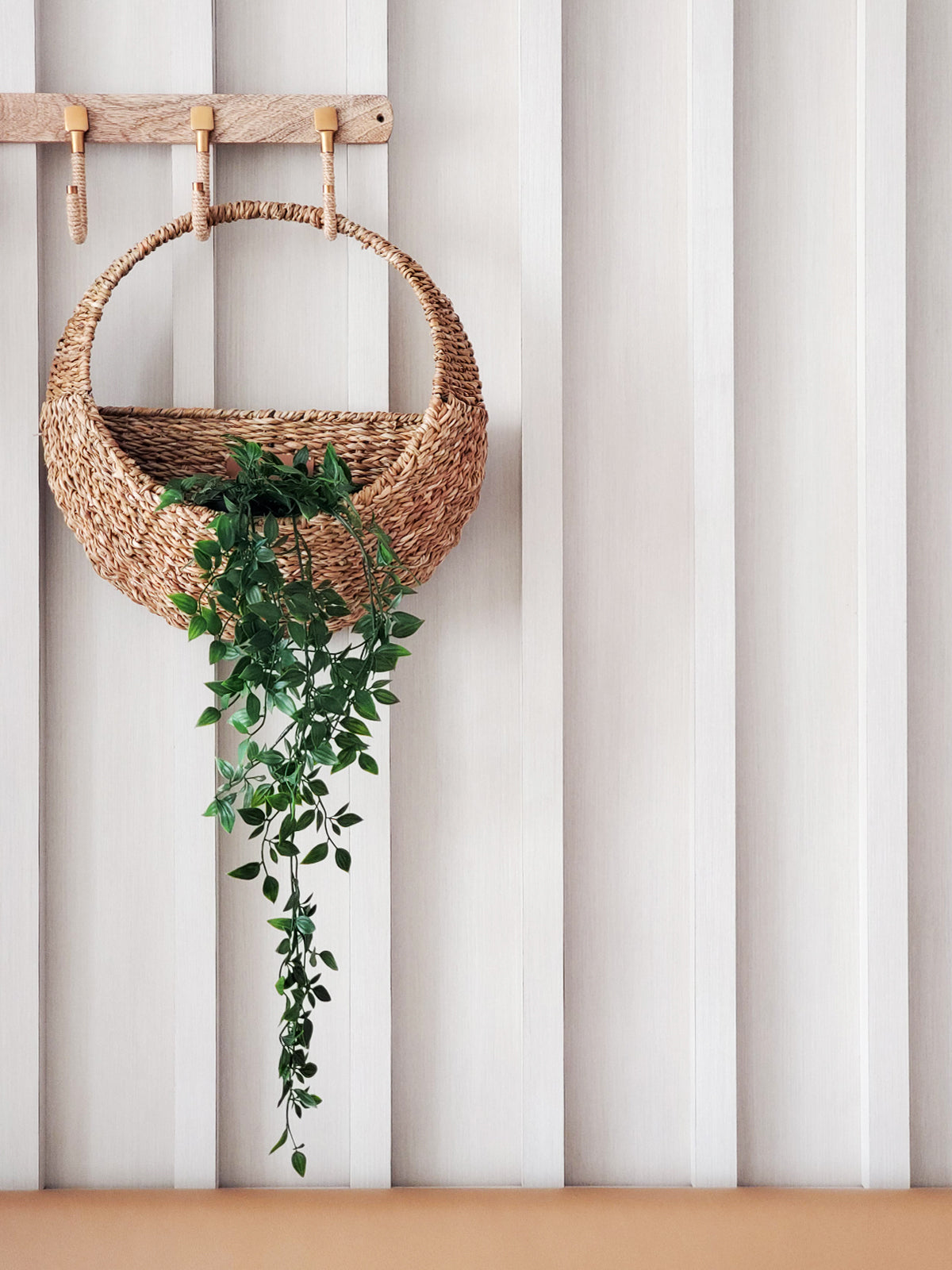 Handwoven seagrass wall hanging basket with a trailing plant on a white slat wall