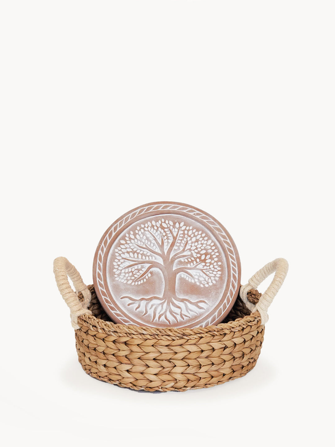 Round terracotta bread warmer with a Tree of Life design in a woven seagrass basket