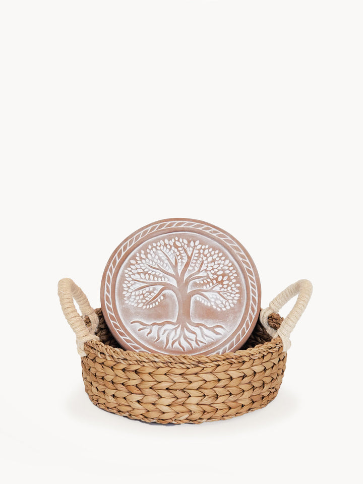 Round terracotta bread warmer with a Tree of Life design in a woven seagrass basket