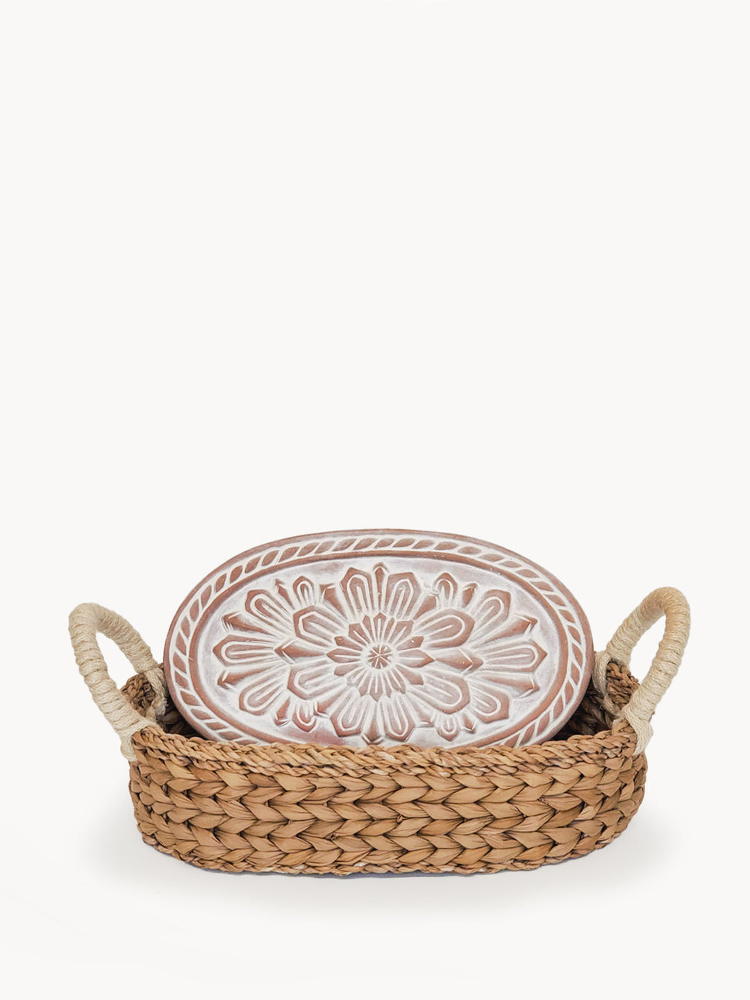 Oval terracotta bread warmer engraved with a flower design in a woven seagrass basket