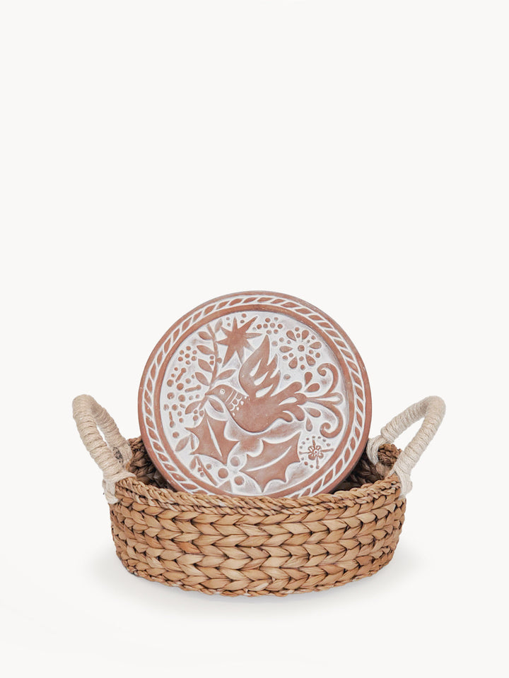 Round terracotta bread warmer engraved with a bird design in a woven seagrass basket
