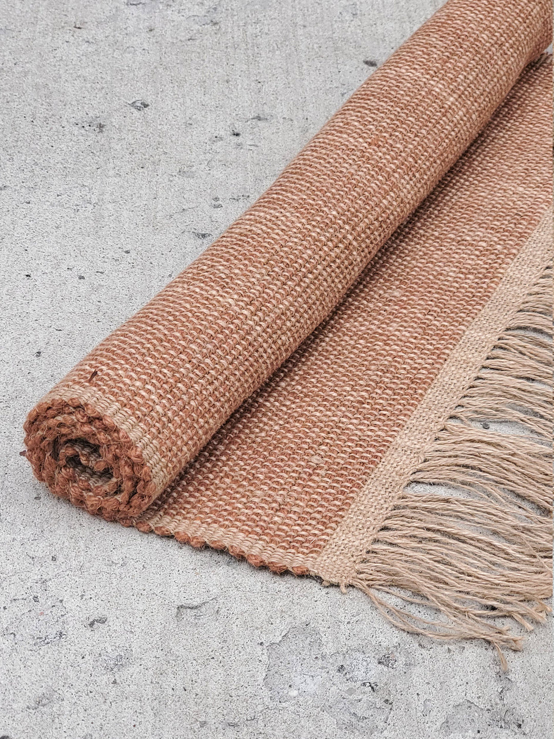 Brown braided jute rug shown on a wooden floor for scale