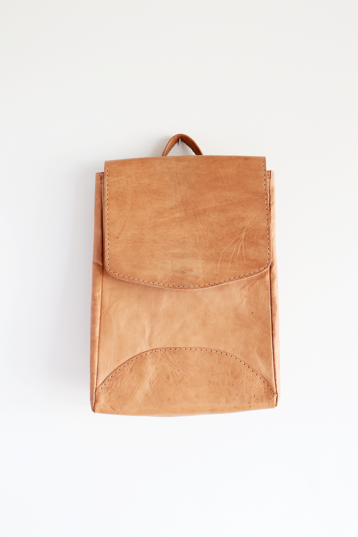 Small leather backpack with adjustable straps, on a plain background.