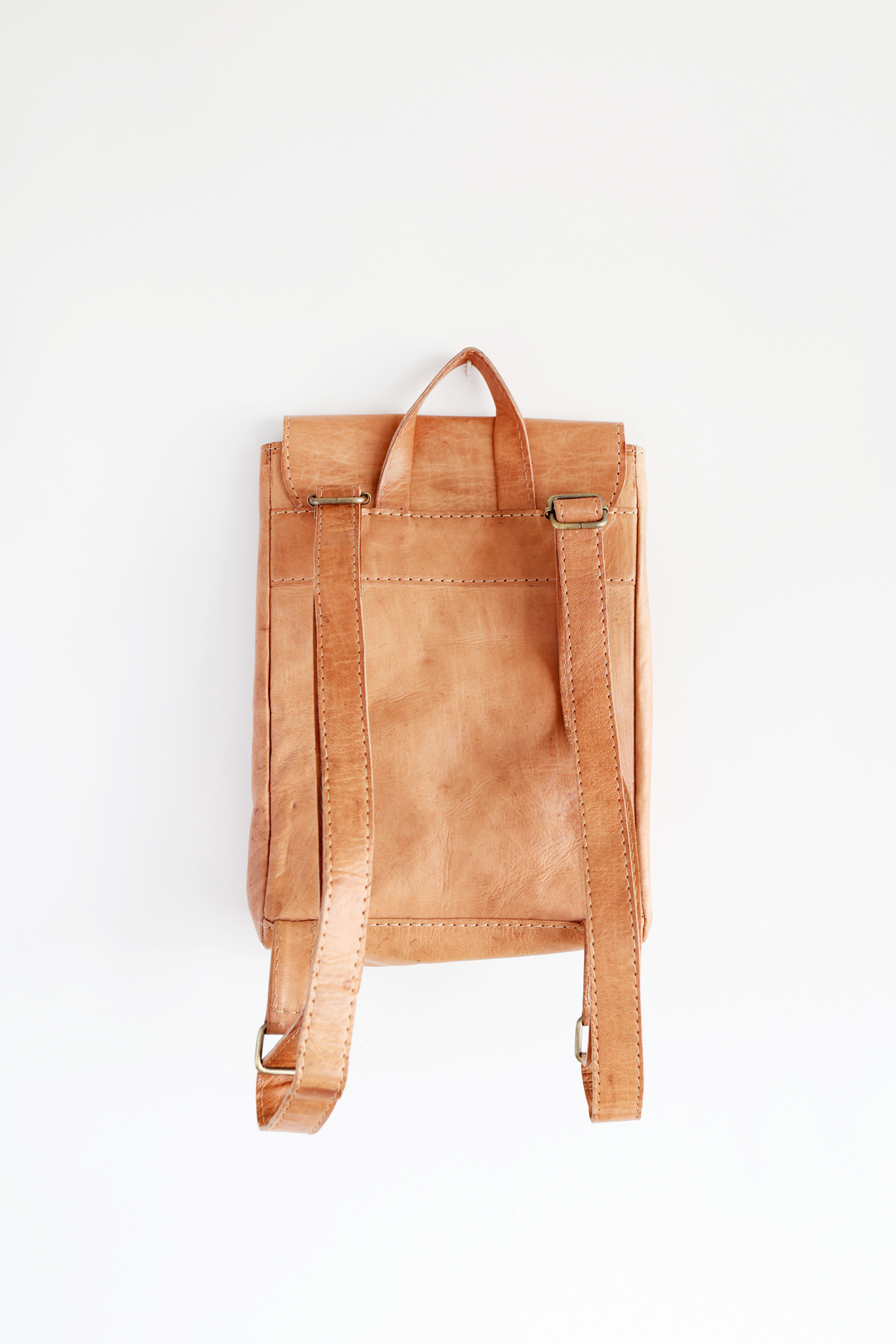 Small leather backpack with adjustable straps and brass side snaps.
