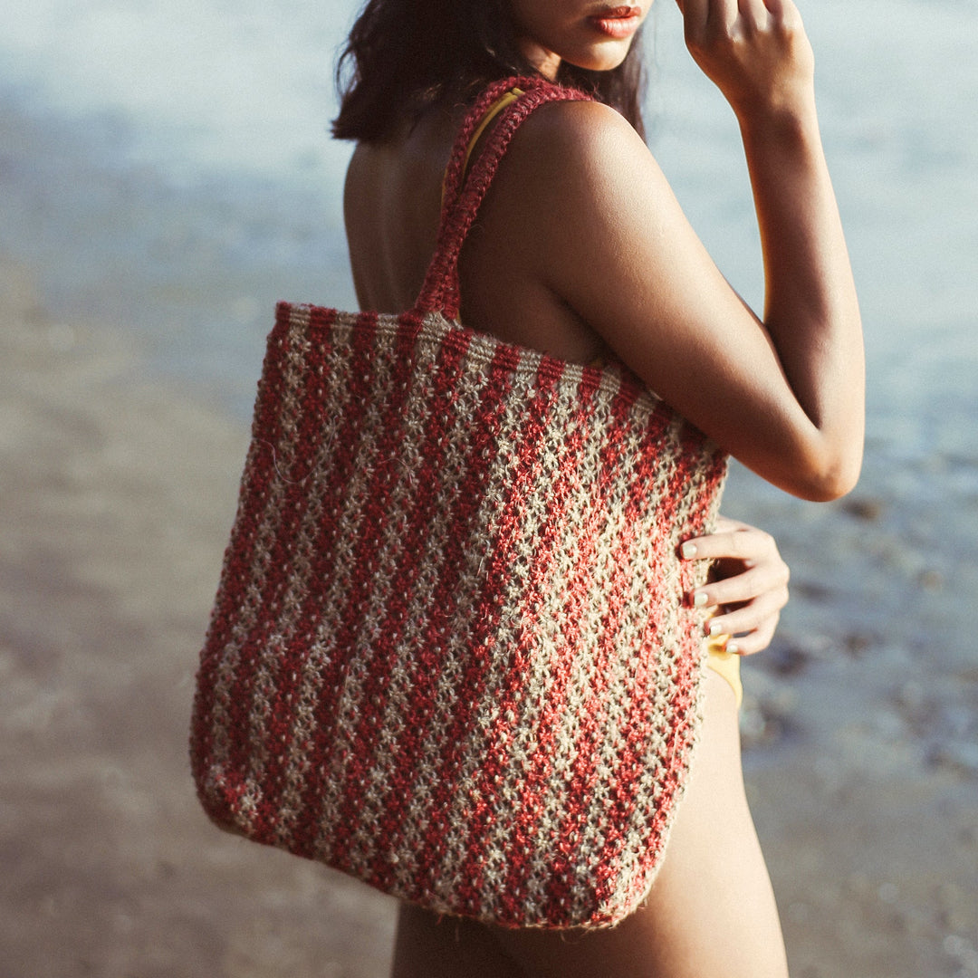 Natural jute striped straw tote bag with two handles, in a casual beach-bag style.