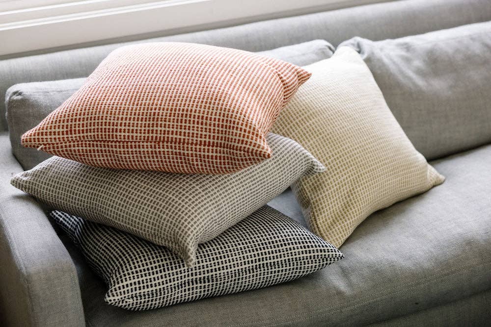 A stack of grid weave cotton pillow covers on a grey sofa in rust, cream and charcoal.