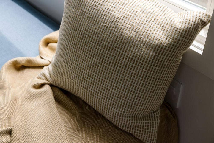 A cream grid weave cotton pillow cover on a window seat with a folded throw.
