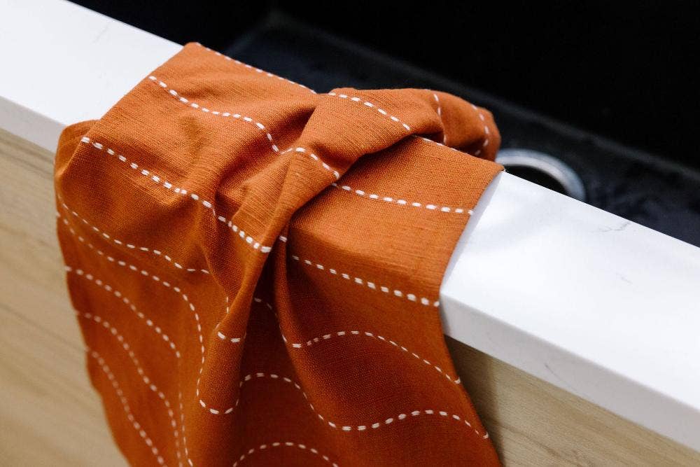 A rust cotton tea towel hung over the edge of a white counter beside a sink.