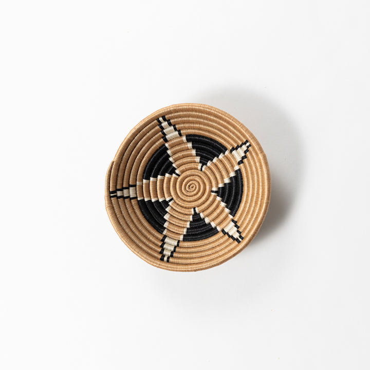Overhead view of a small Boutique Vertex woven bowl in tea-dyed sisal with a black and ivory pinwheel.