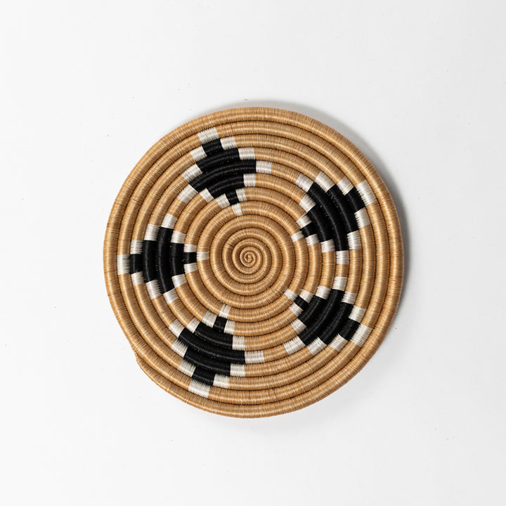 Handwoven sisal trivet with a diamond pattern on a wooden surface.