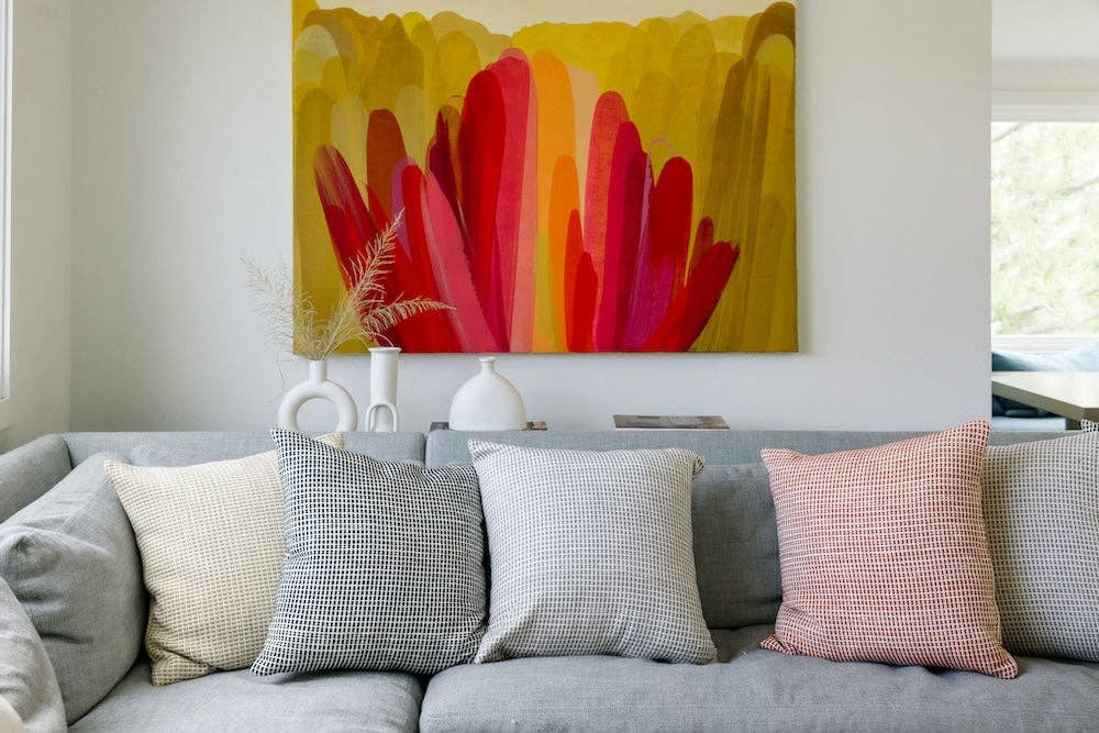 Four grid weave cotton pillow covers along a grey sofa beneath a large abstract painting.