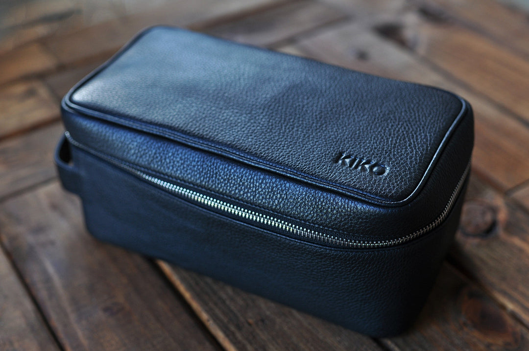 Handcrafted leather dopp kit with a zipper and toiletry compartments on a neutral background.