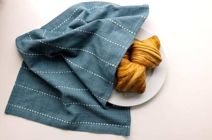 A teal cotton tea towel covering croissants on a white plate.