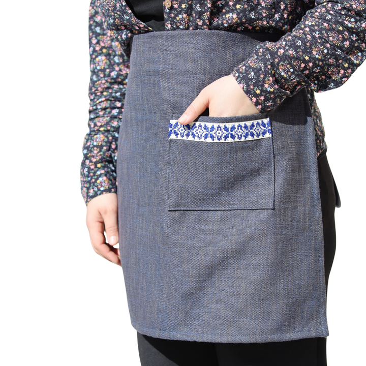 Navy half apron with a hand-embroidered blue-and-white tatreez band on the front pocket.