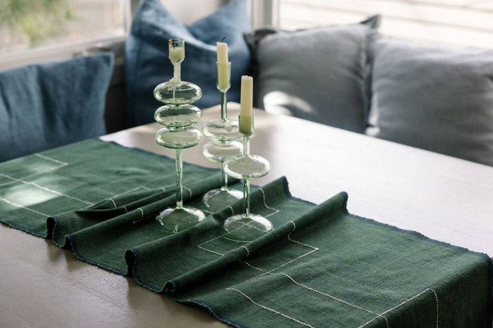 A dark green cotton table runner on a wooden dining table with glass candlesticks.