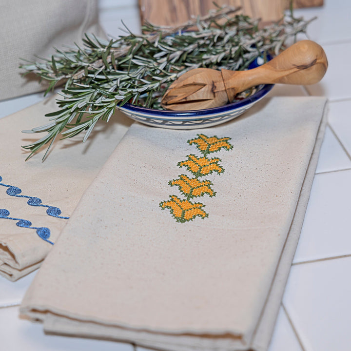 Palestinian tatreez tea towel, a column of yellow cross-stitch blooms with green stems on unbleached cotton.