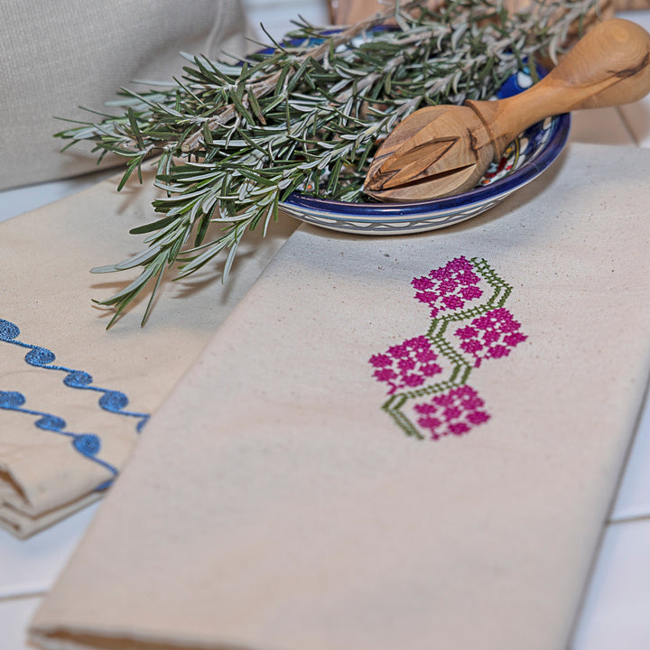 Palestinian tatreez tea towel showing fuchsia grape clusters on a green vine, on unbleached cotton.
