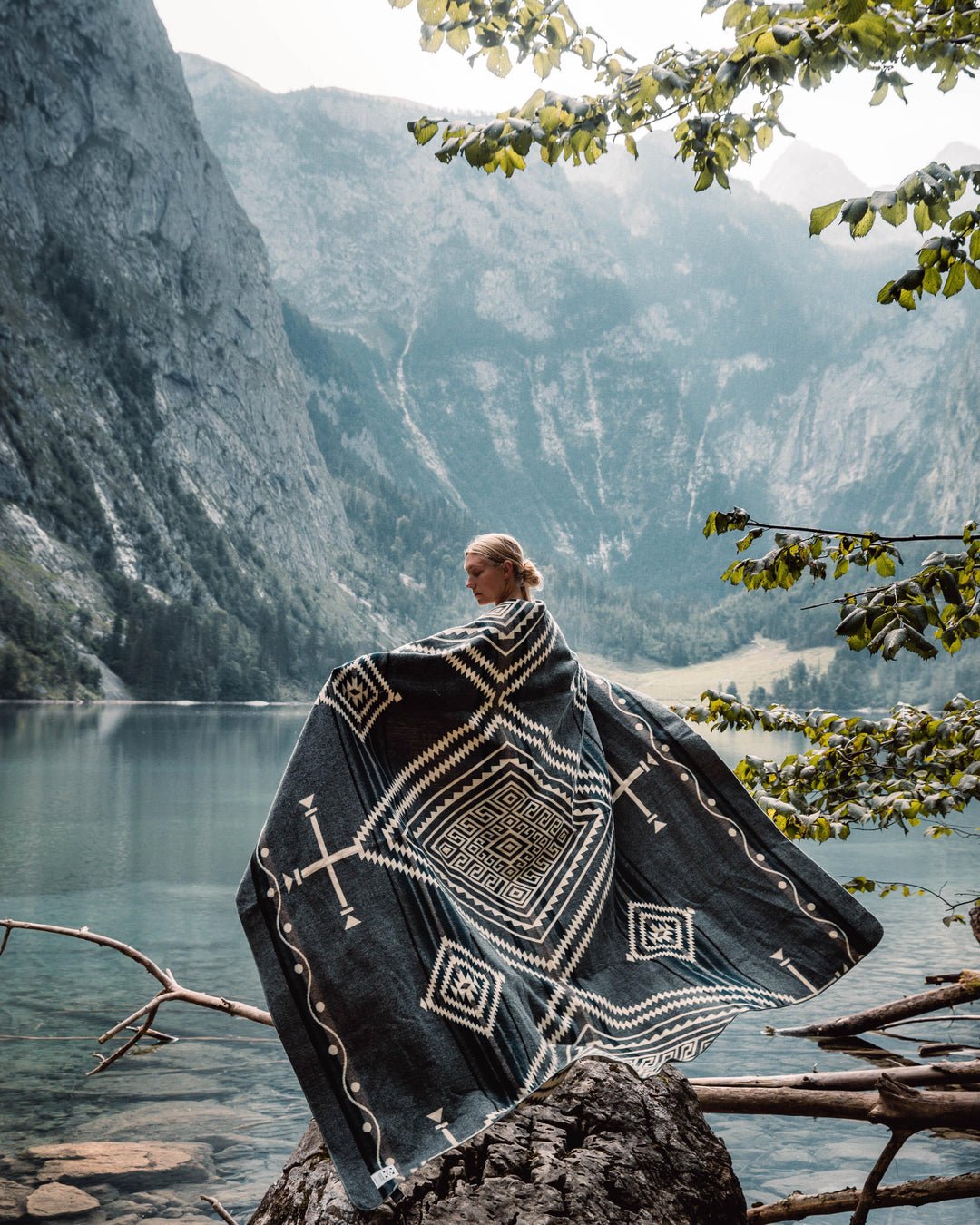 Achuar Ash Grey reversible blanket showing the cream side with soft grey geometric pattern, draped over a rattan chair.