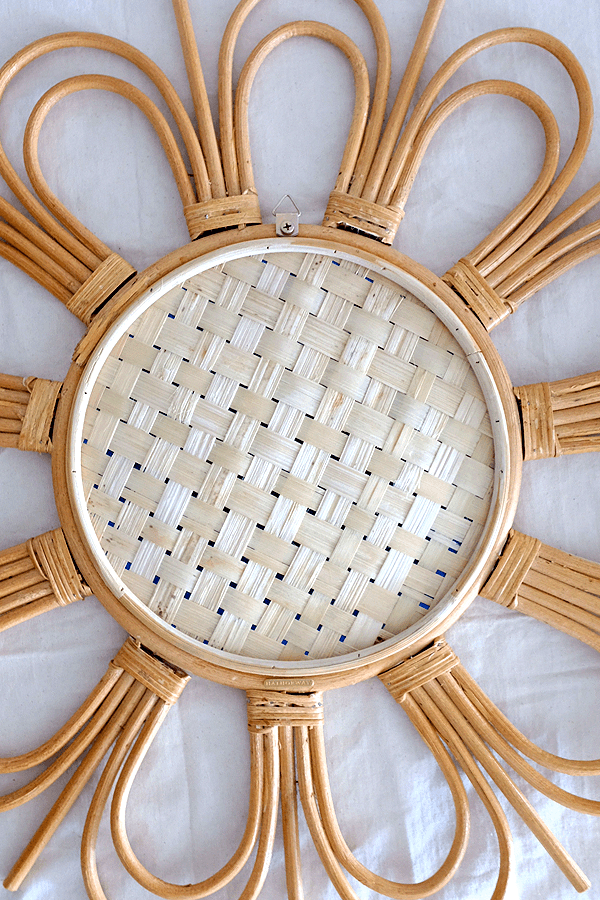 Sunburst rattan mirror with a flower-shaped frame and round reflective surface.