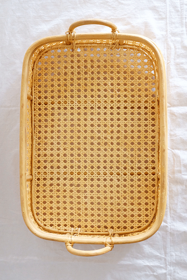 Handwoven rattan tray with cane weaving and handles, for serving or decor.