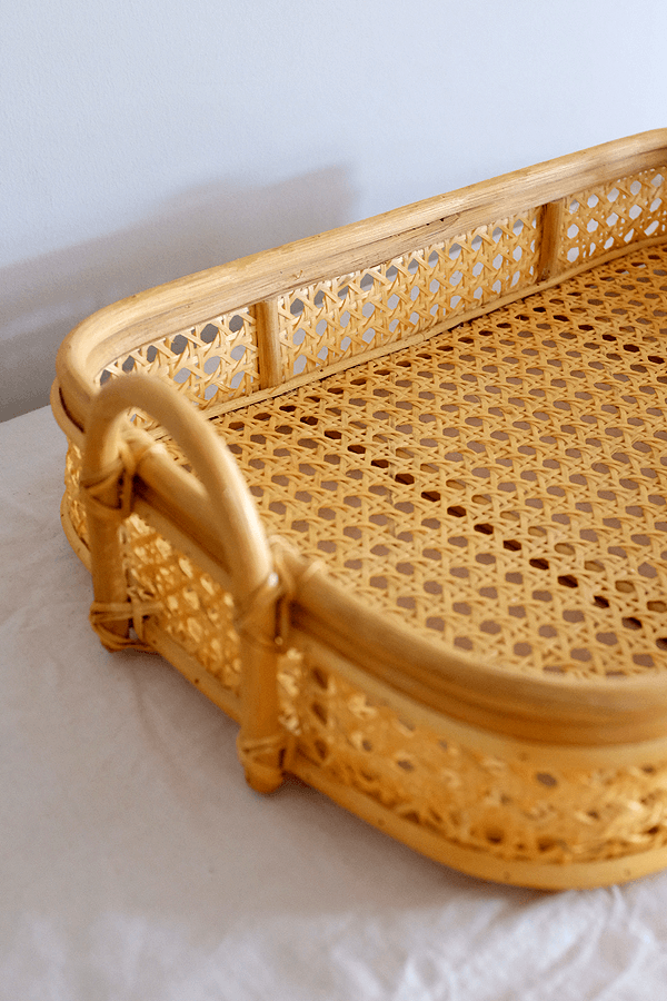 Handwoven rattan tray with handle openings and a cane design, for serving or decor.