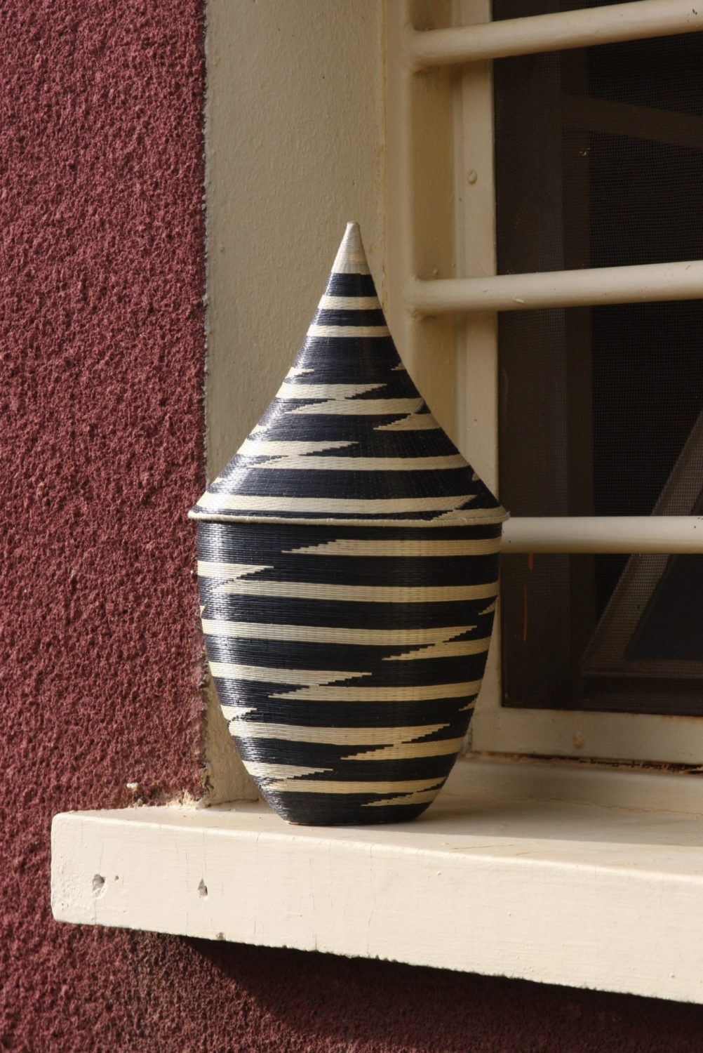 Black and white handwoven grass peace basket with intricate umuraza weaving.