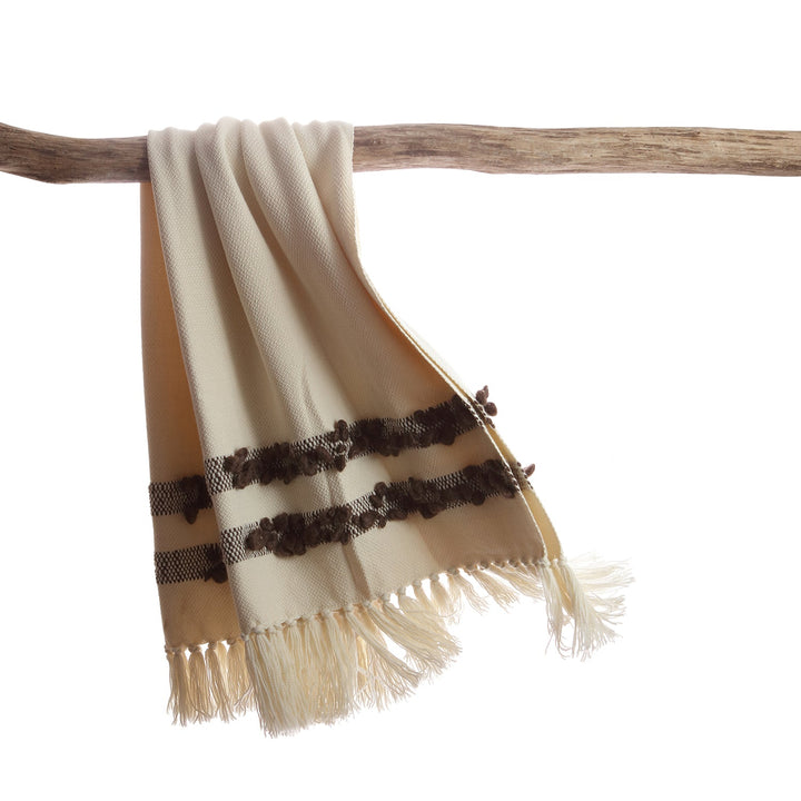 Ivory merino wool throw with brown bobbled bands hanging over a driftwood branch.