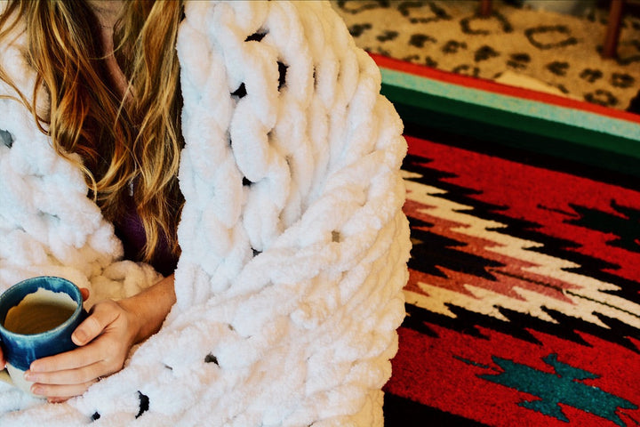 White chunky knit chenille throw blanket draped over a sofa.