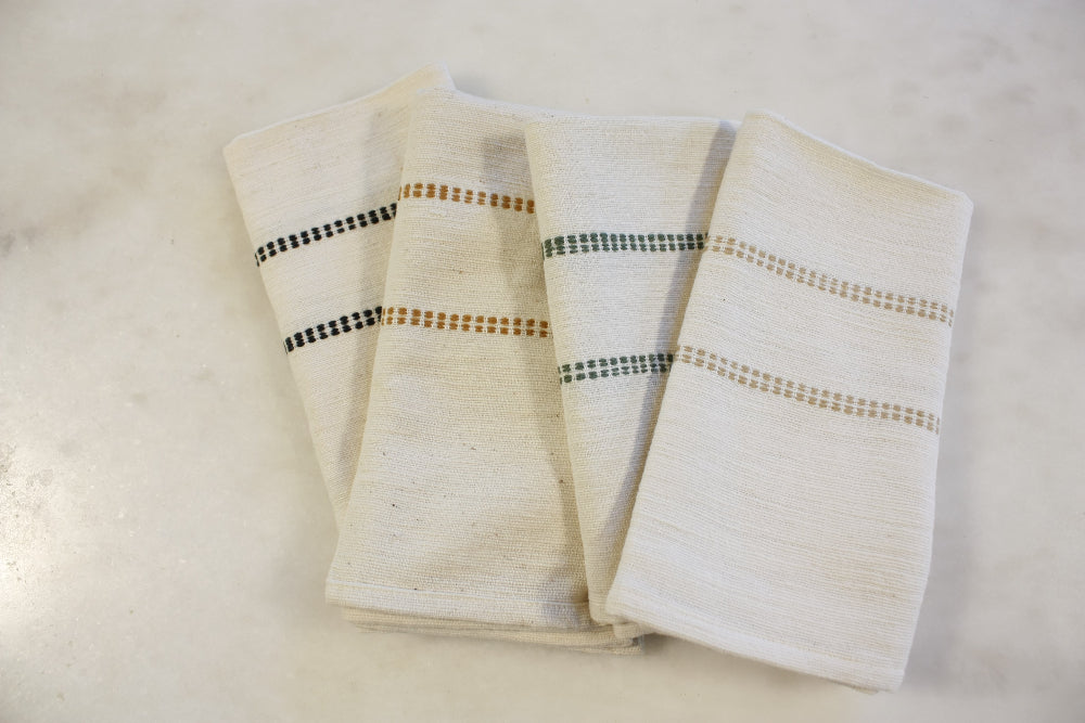 Four natural cotton napkins with black, bronze, almond and cedar check bands on a marble table