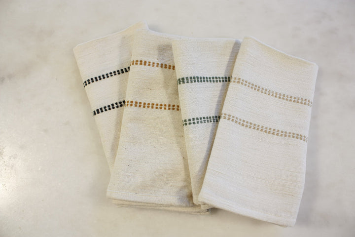 Four natural cotton napkins with black, bronze, almond and cedar check bands on a marble table