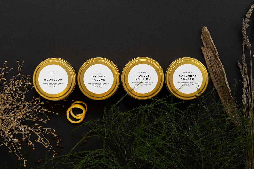 Four brushed gold tin candles from the Cozy Collection with a branded scent card.