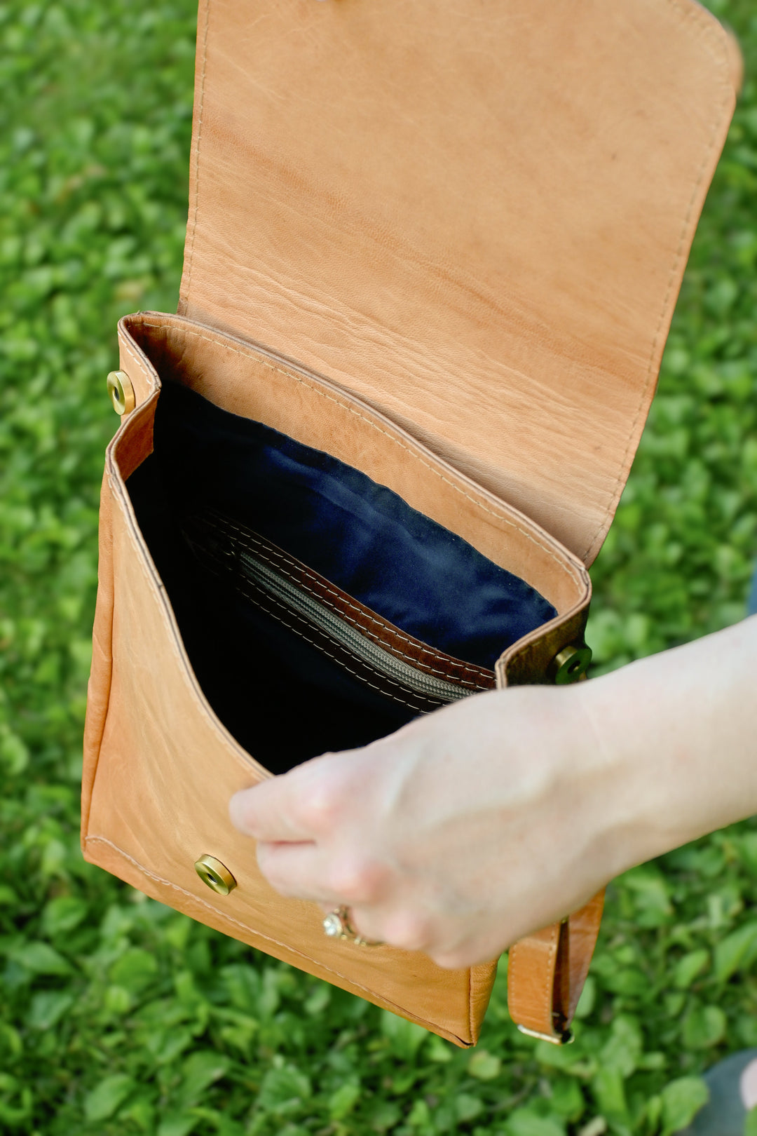 Small leather backpack with a brass magnetic closure, on a wooden surface.