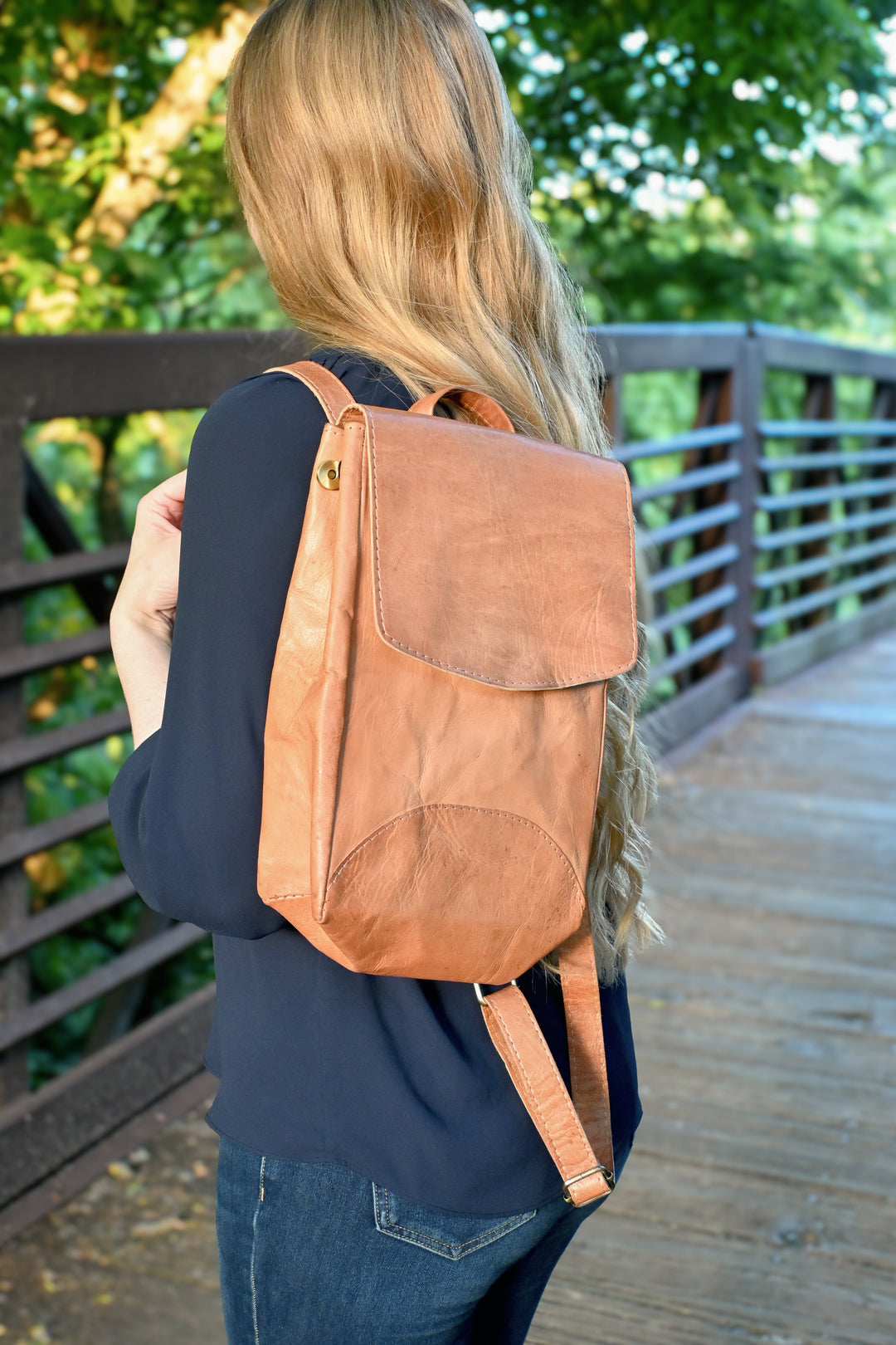 Small handmade leather backpack with brass snaps, on a wooden surface.