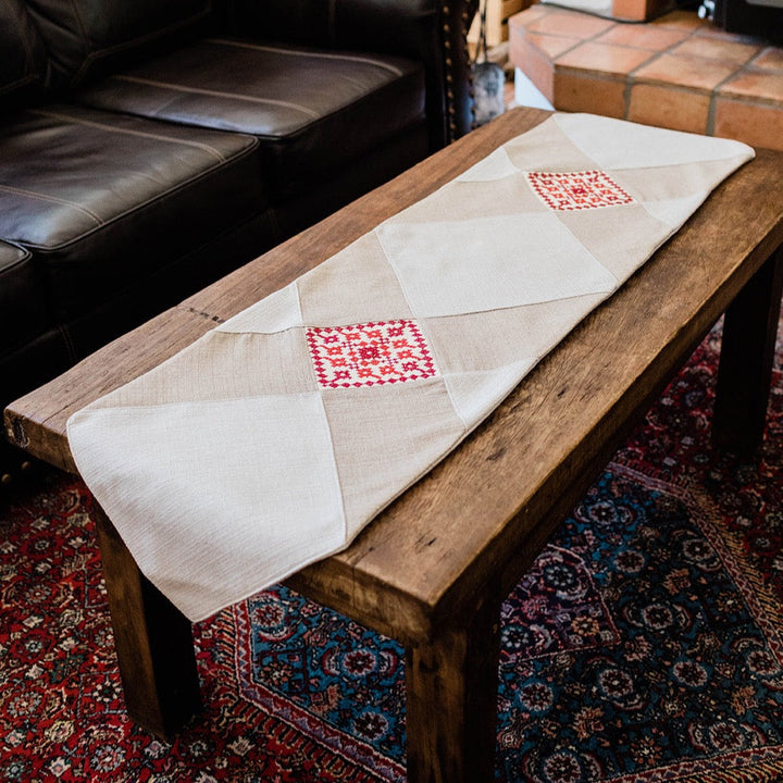 Hand-embroidered natural table runner with red Palestinian tatreez, on a wooden table.