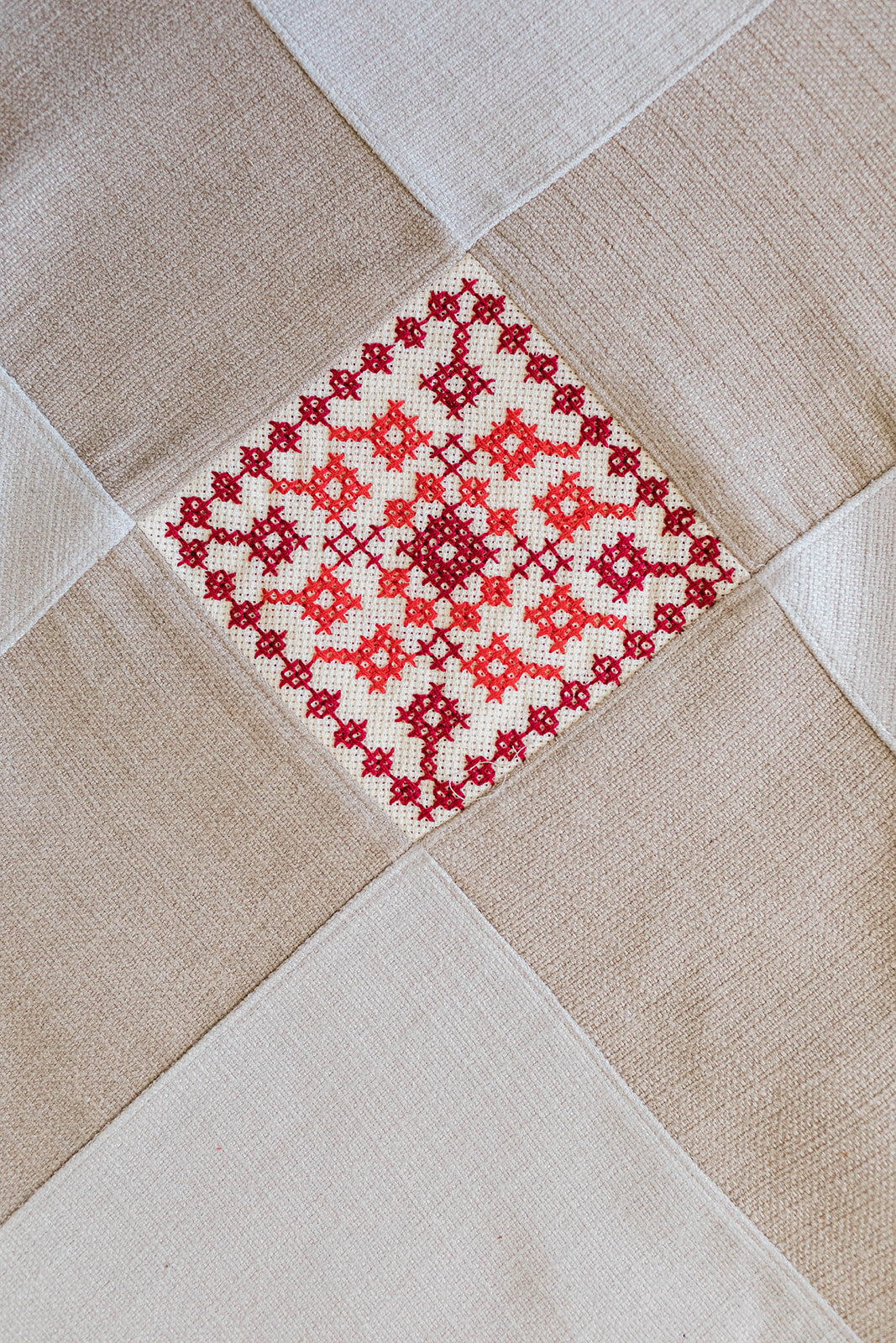 Natural linen table runner with two red tatreez diamond motifs and pointed ends.