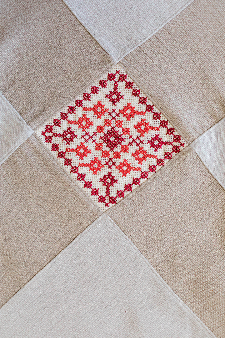 Natural linen table runner with two red tatreez diamond motifs and pointed ends.