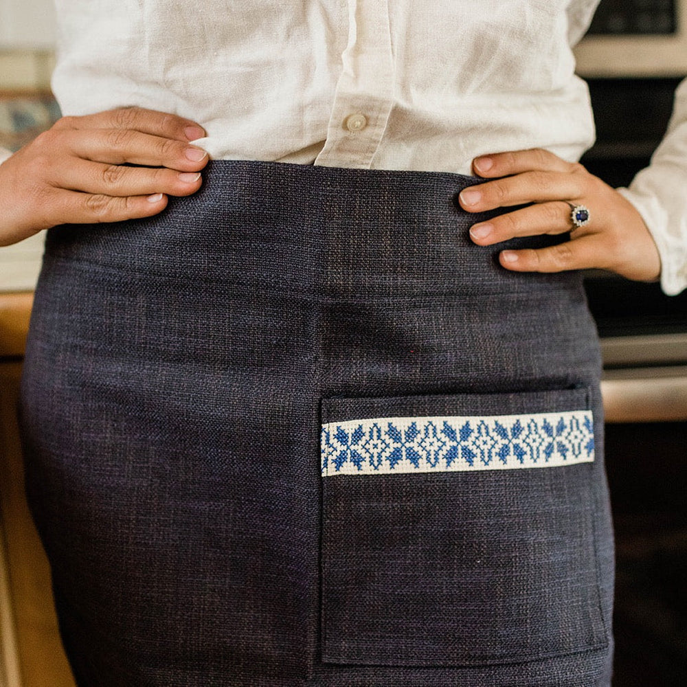 Navy cotton waist apron with a blue-and-white Sea tatreez band and a front pocket.