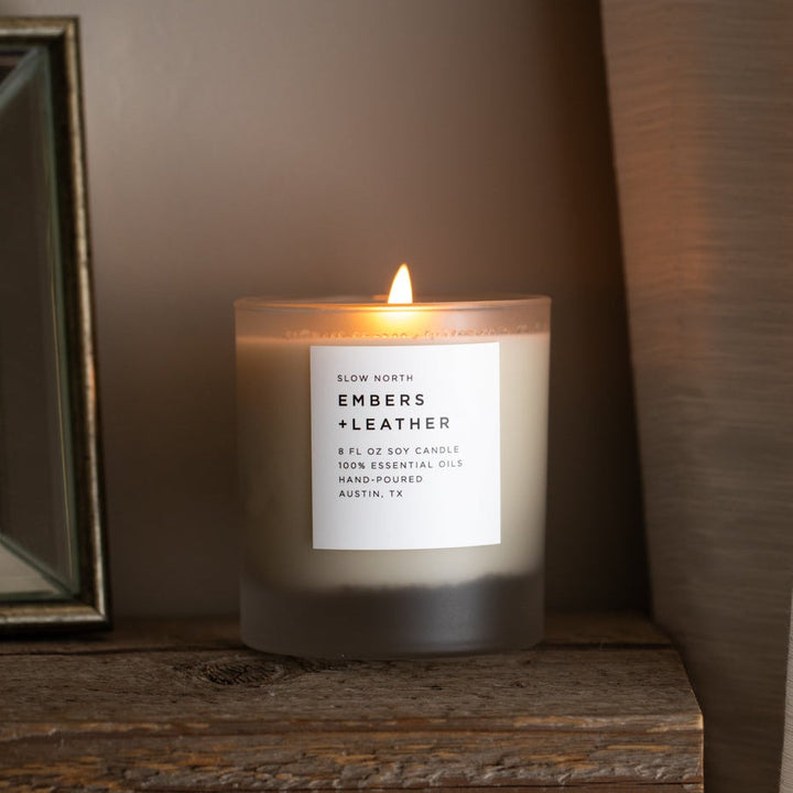 Embers &amp; Leather signature candle with burning flame and leather-wrapped lid.