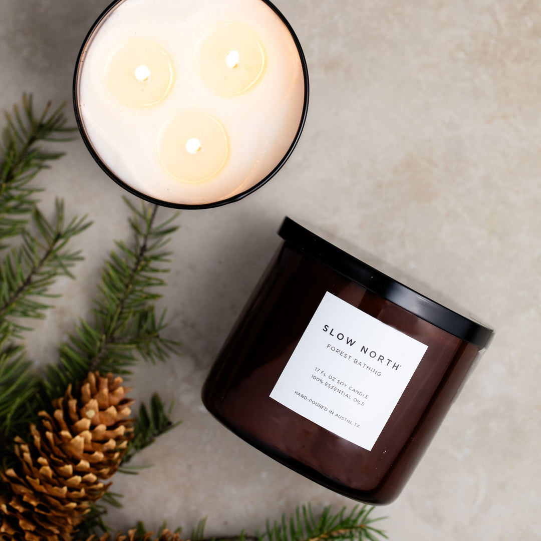 Forest Bathing three-wick candle with lush forest design and warm glow.