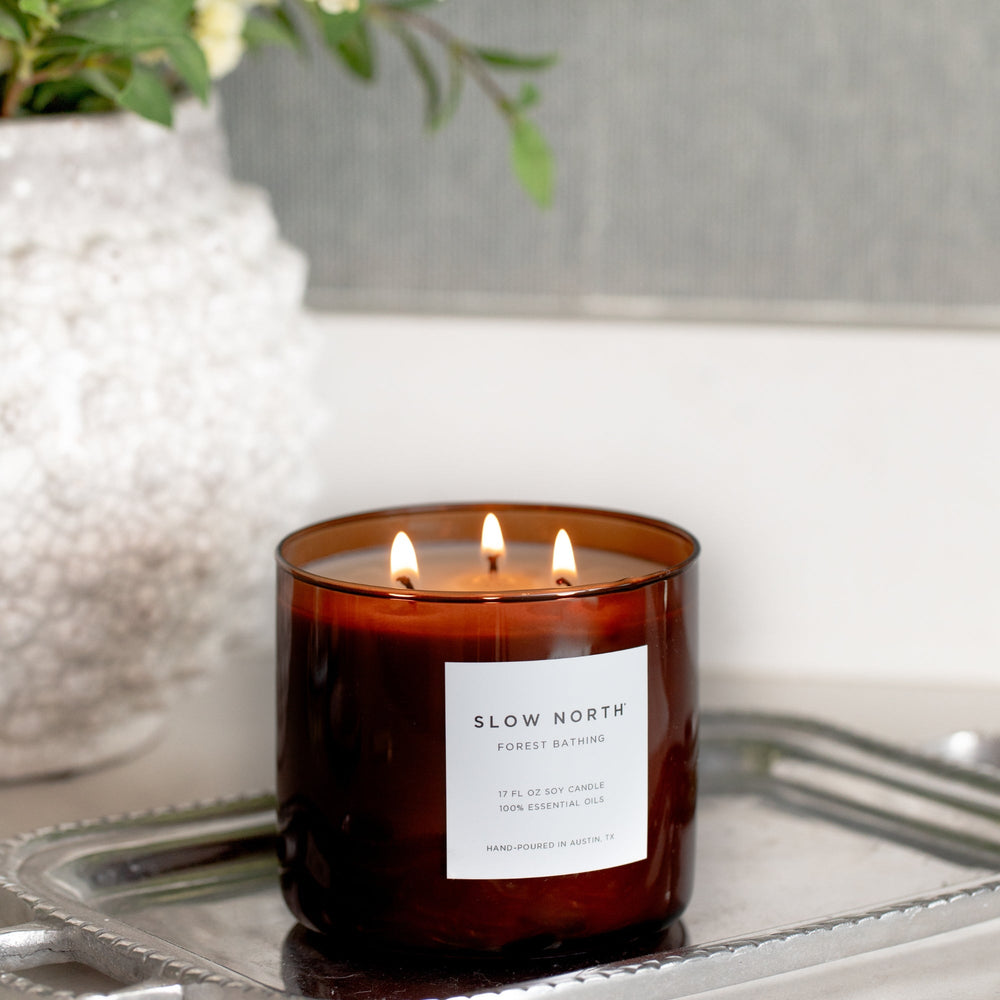 Forest Bathing three-wick candle with botanical accents and warm glow.
