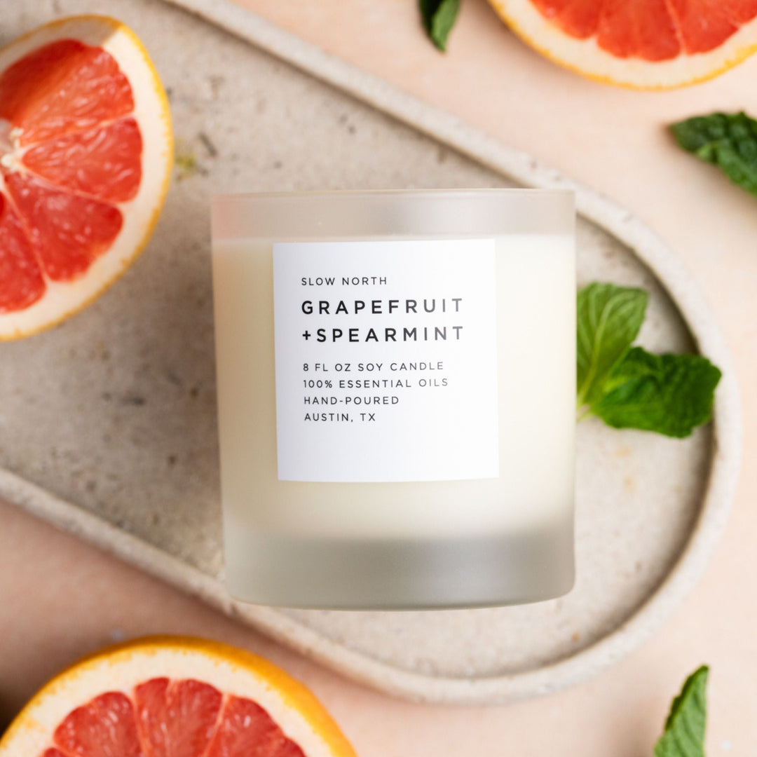 Glass jar candle with grapefruit and spearmint scent and lit flame.