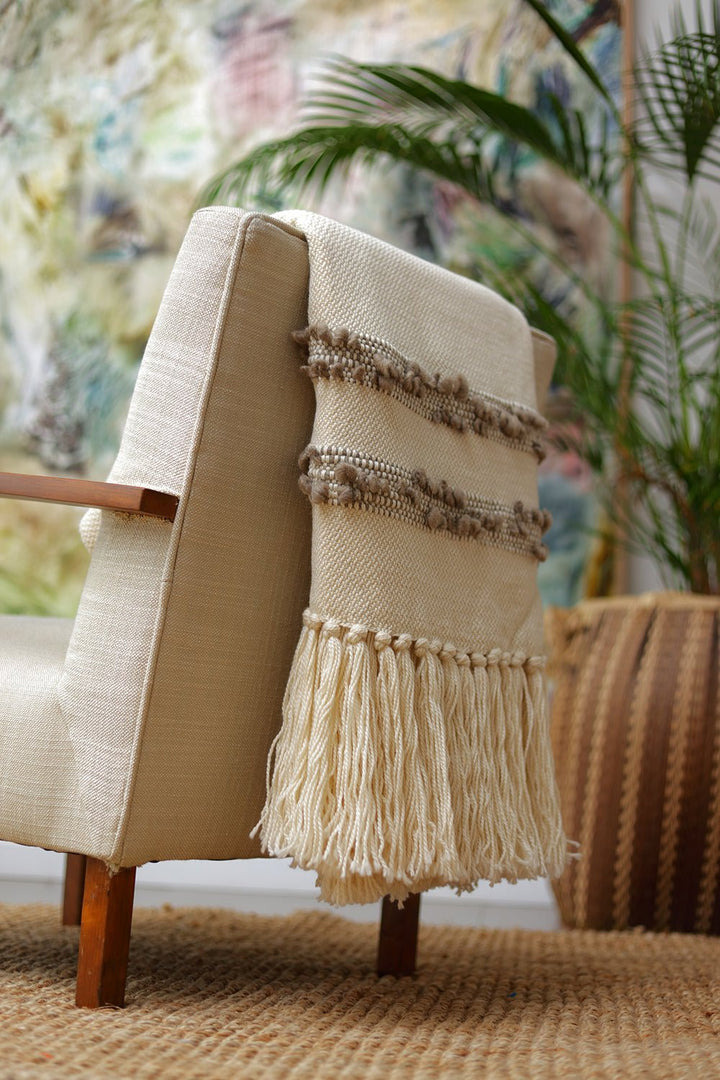 Ivory merino wool throw with taupe bobbled bands and long fringe, draped over the back of a linen armchair.