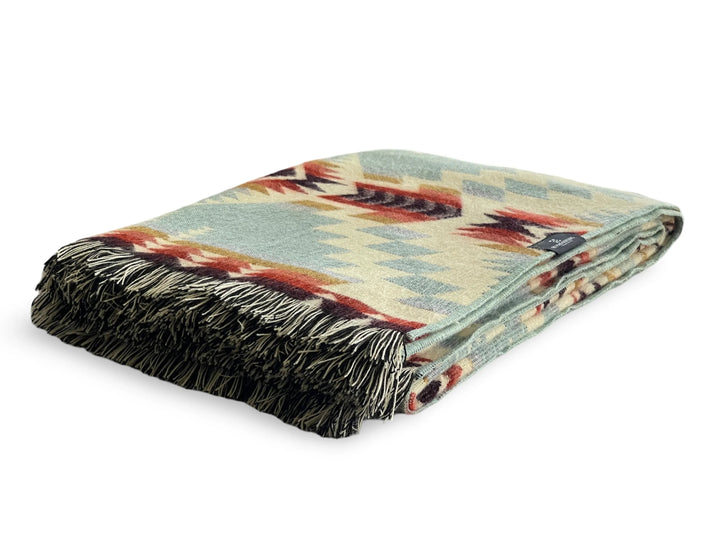 Handwoven Andean fringed throw in sage and teal with cream, rust, and maroon, draped over a chair.
