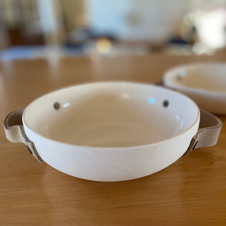 Handmade ceramic bowl with leather handles, textured ceramic with leather accents.